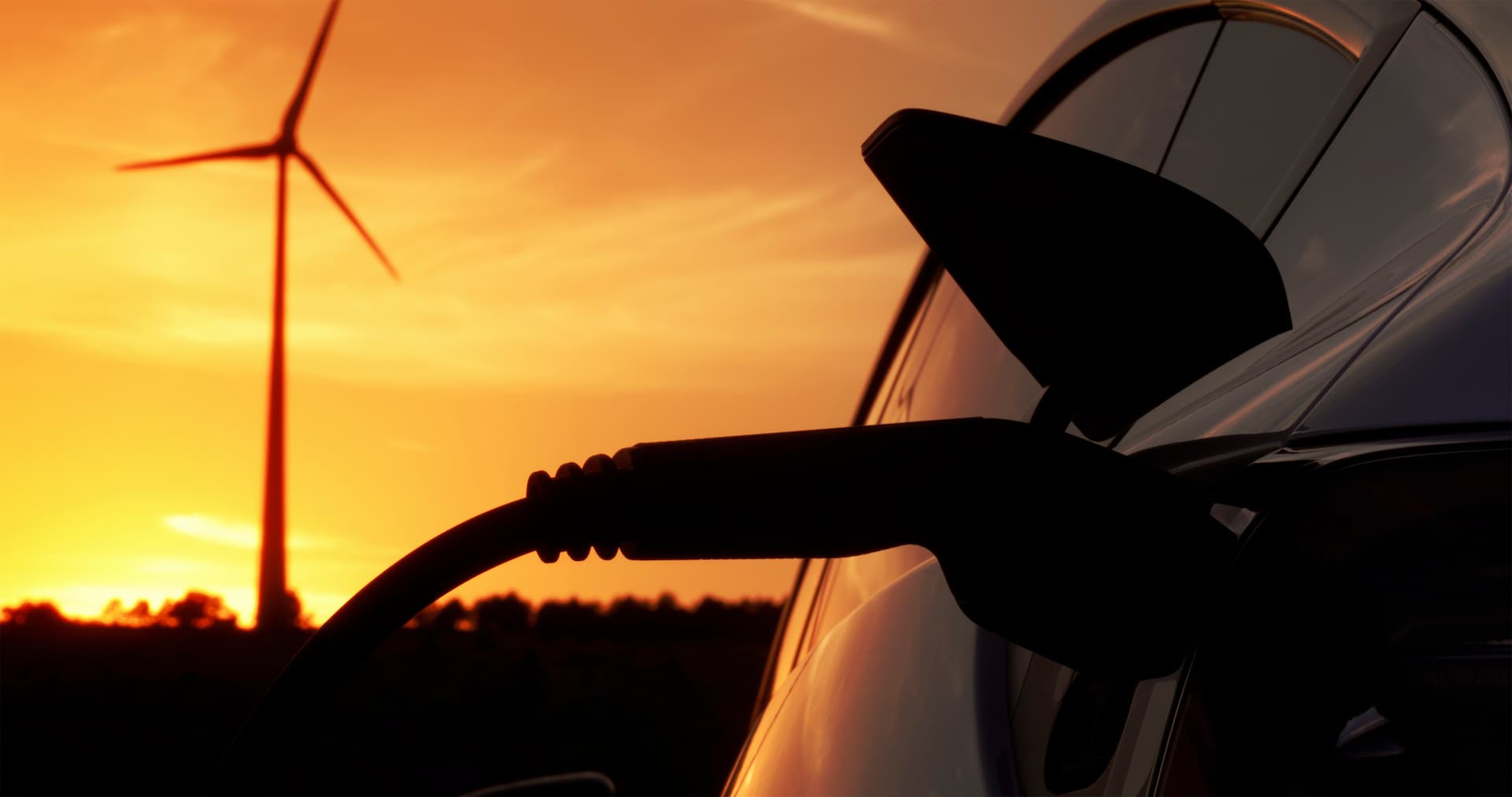 Electric car being charged with wind turbine in the background